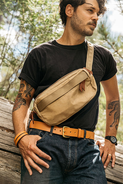 Saddle tan leather belt with a brass buckle, worn by a man in dark jeans and a black t-shirt.