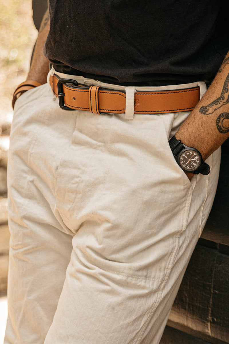 Saddle Tan leather belt with a black buckle and contrast stitching, worn with light beige pants.