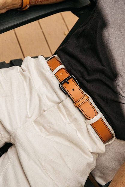Saddle Tan leather belt with black stitching and a dark buckle, worn with a white linen shirt and gray pants.