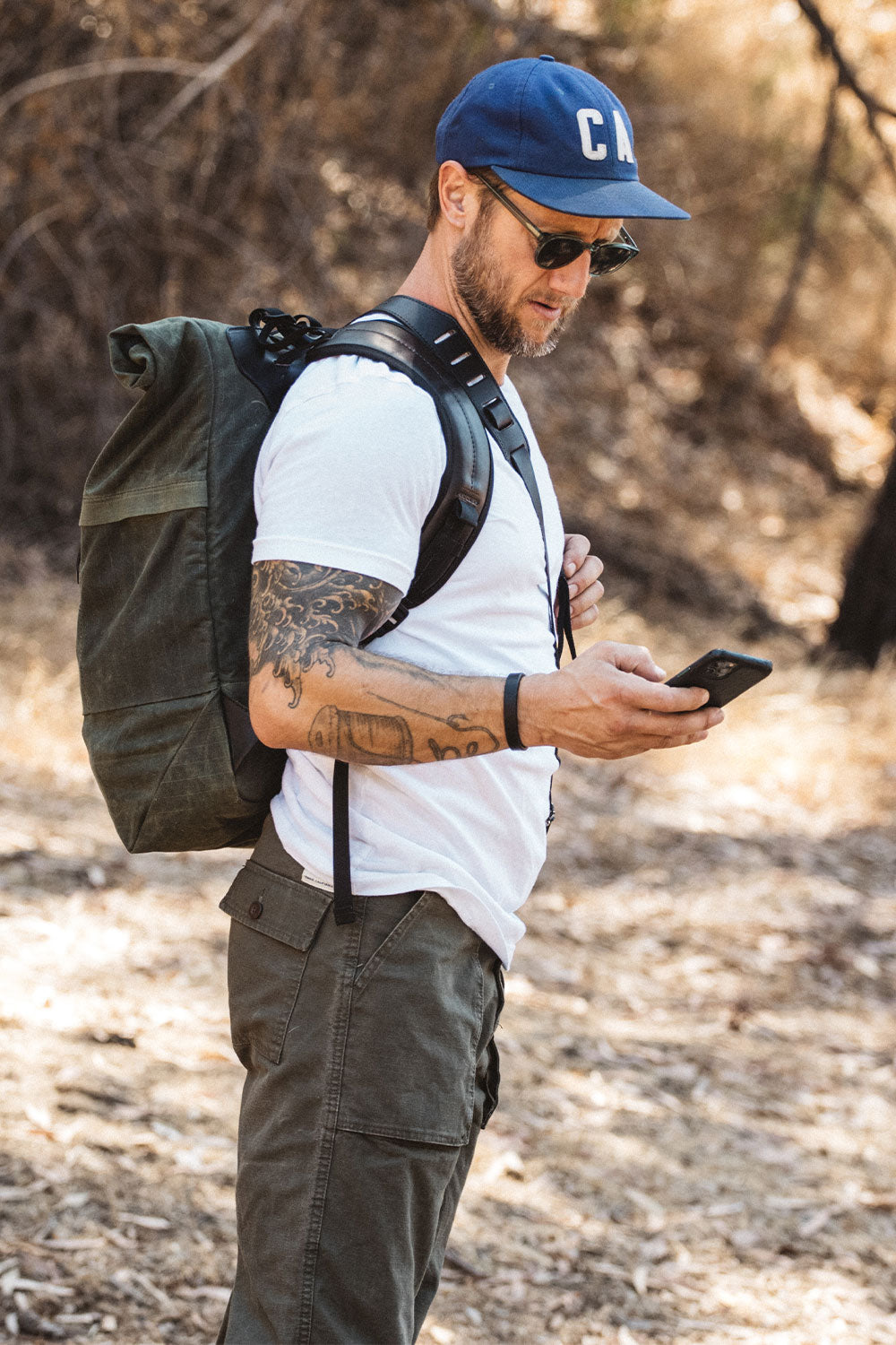Black single wrap wristband on a man's tattooed left wrist, worn with a white t-shirt outdoors.
