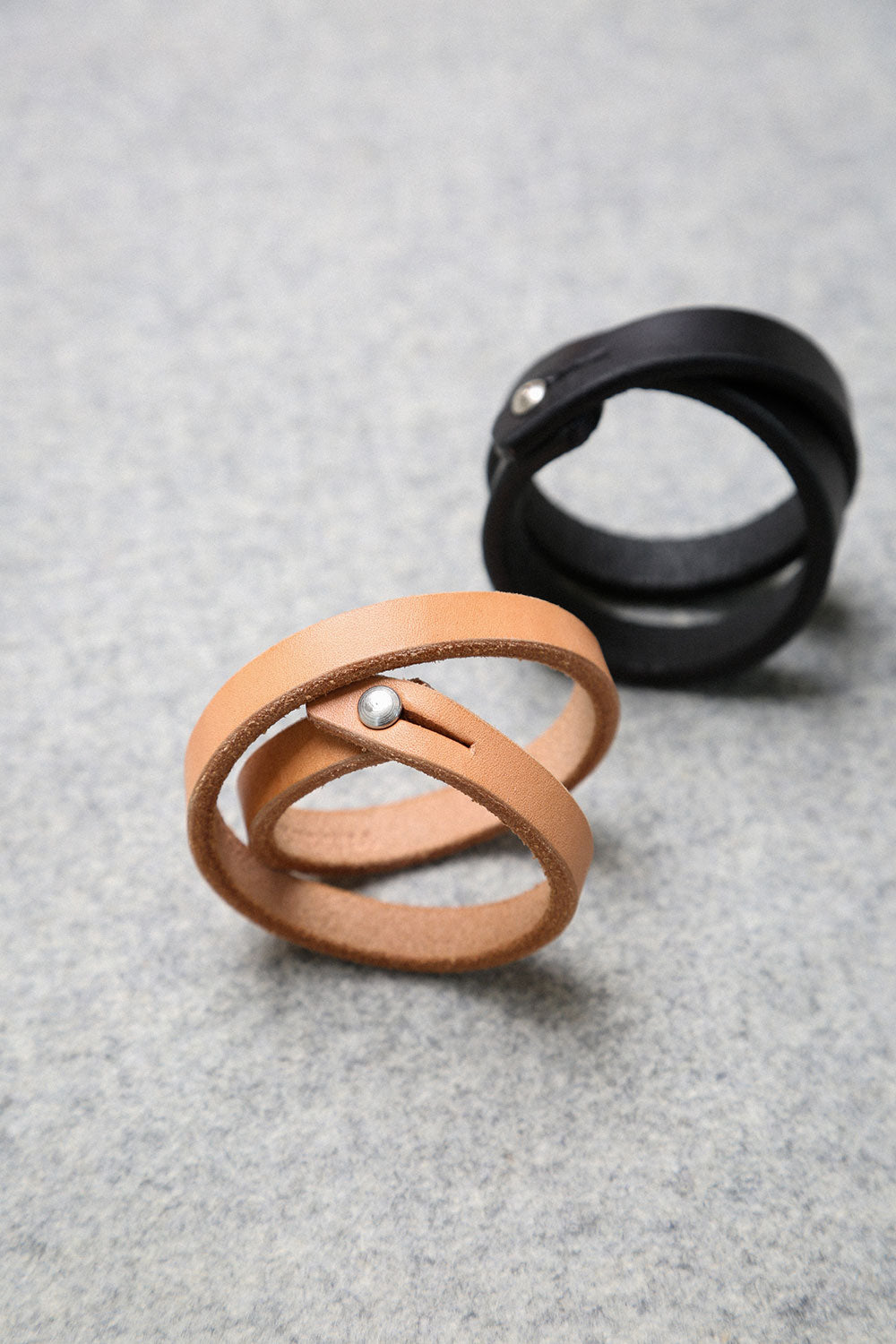 Natural single wrap leather wristband with a silver stud, with a black wristband blurred in the background.