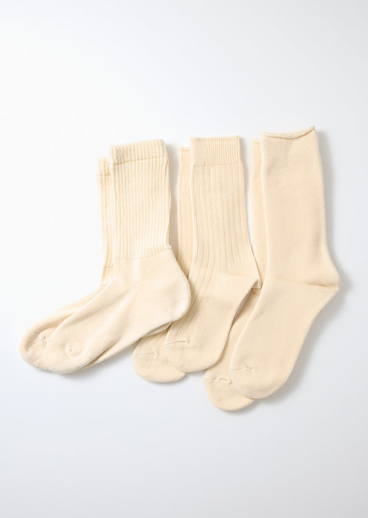 Three pairs of ecru knit crew socks featuring ribbed legs, laid flat on a white surface.
