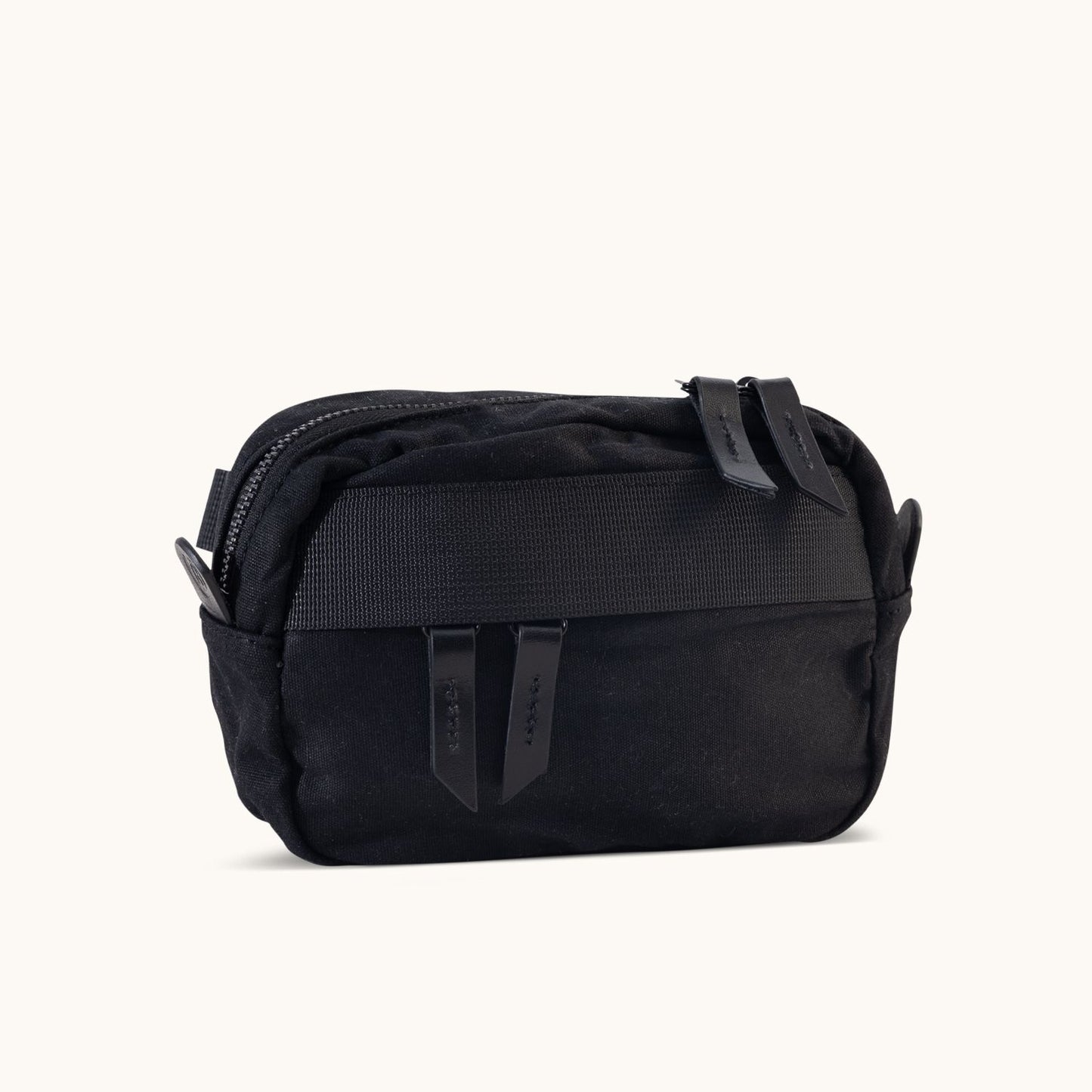 Black waxed canvas Canyon Crossbody Mini with a top zipper, two leather pulls, and a textured front strap.