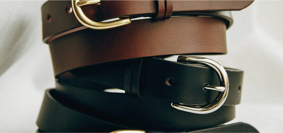 Stacked leather belts in brown and black with gold and silver buckles, arranged vertically against a white background.