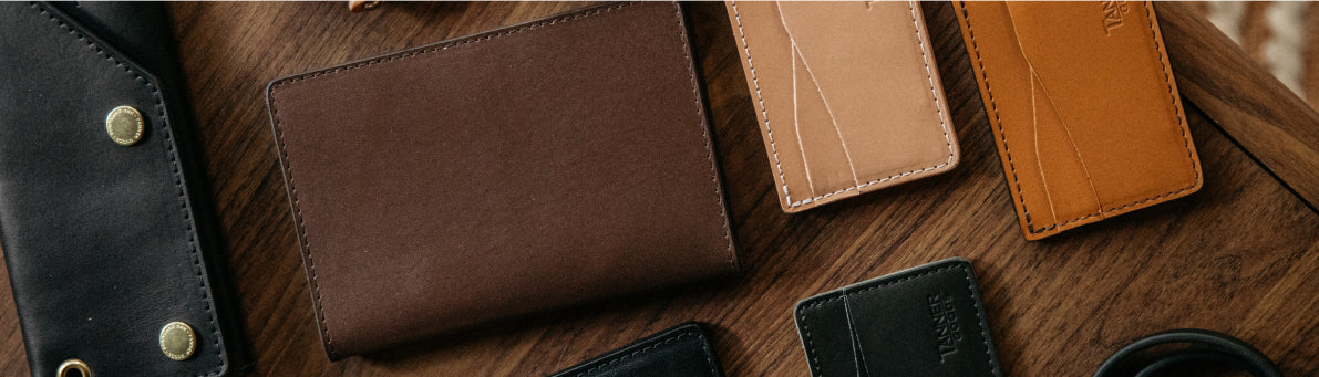 Brown leather wallets and cardholders arranged on dark wood surface, featuring stitching and brand embossing.