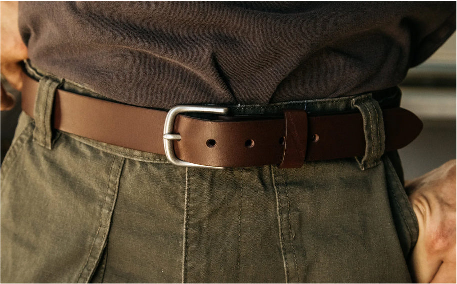 Brown leather belt with silver buckle worn with olive green pants and dark shirt, close-up view.