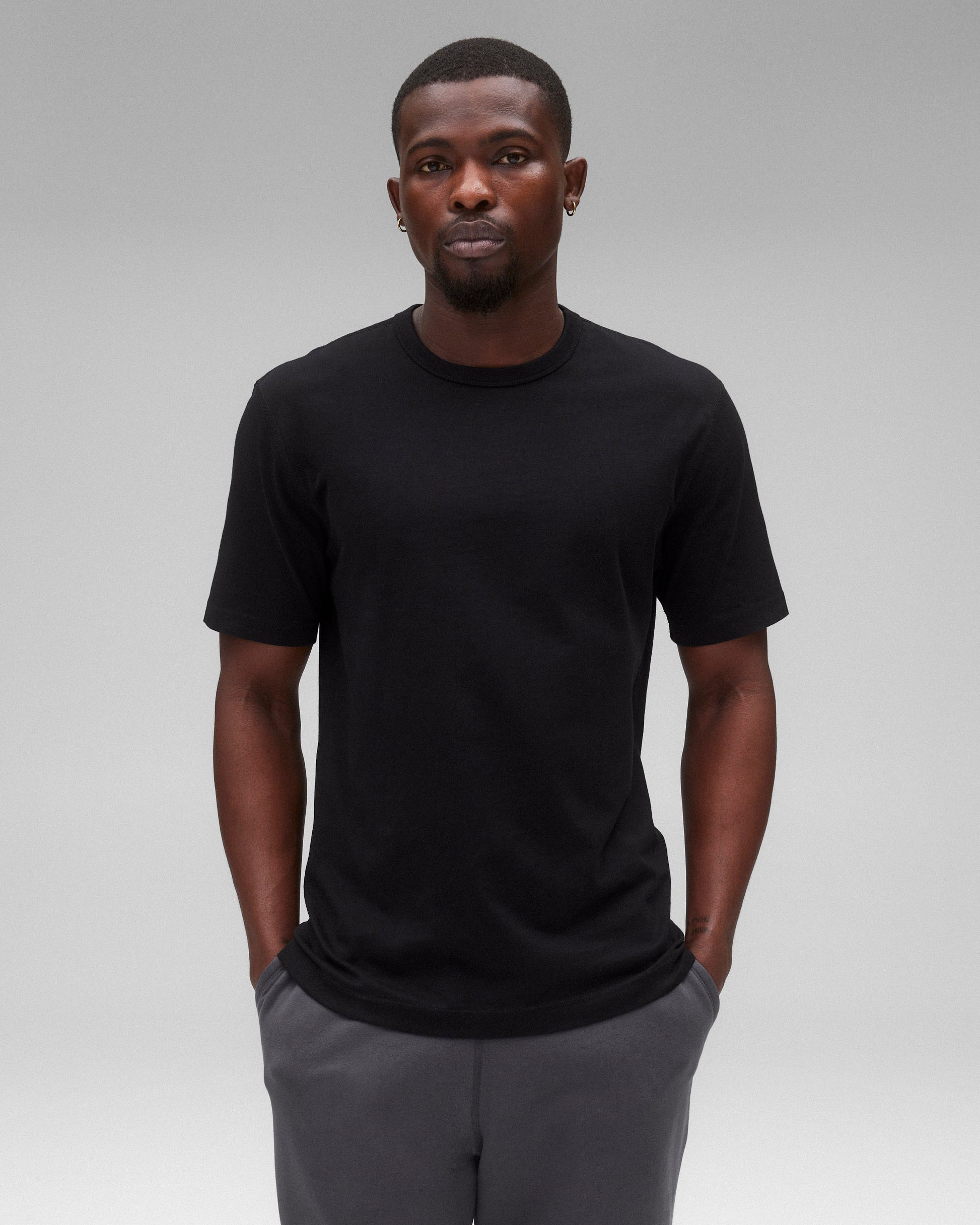 Black Lightweight Jersey Standard T-Shirt, crew neck, short sleeves, worn by a man with hands in pockets and dark grey joggers.