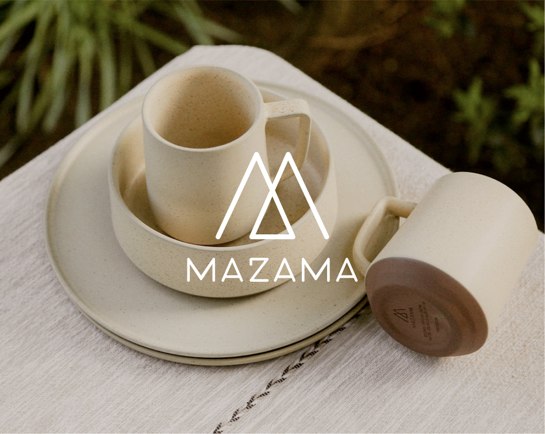 Beige ceramic mugs and plates stacked on a textured white cloth, with greenery in the background and "MAZAMA" logo overlaid.