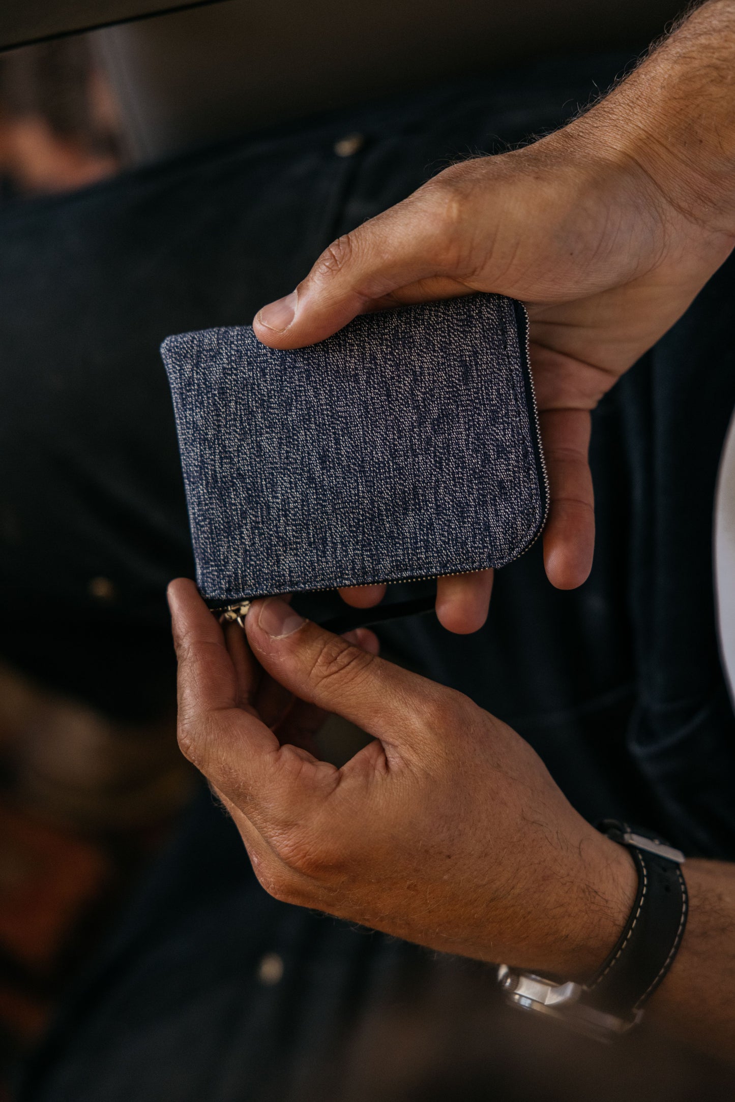 Indigo salt and pepper textile universal zip wallet, held by hands wearing a watch, featuring a zipper.