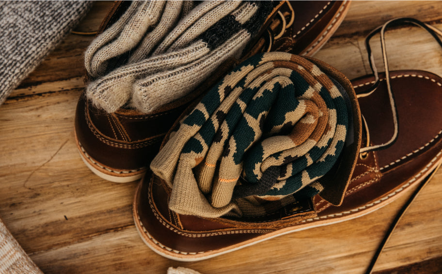 Brown leather boots with patterned socks inside, arranged on wooden surface, warm lighting.
