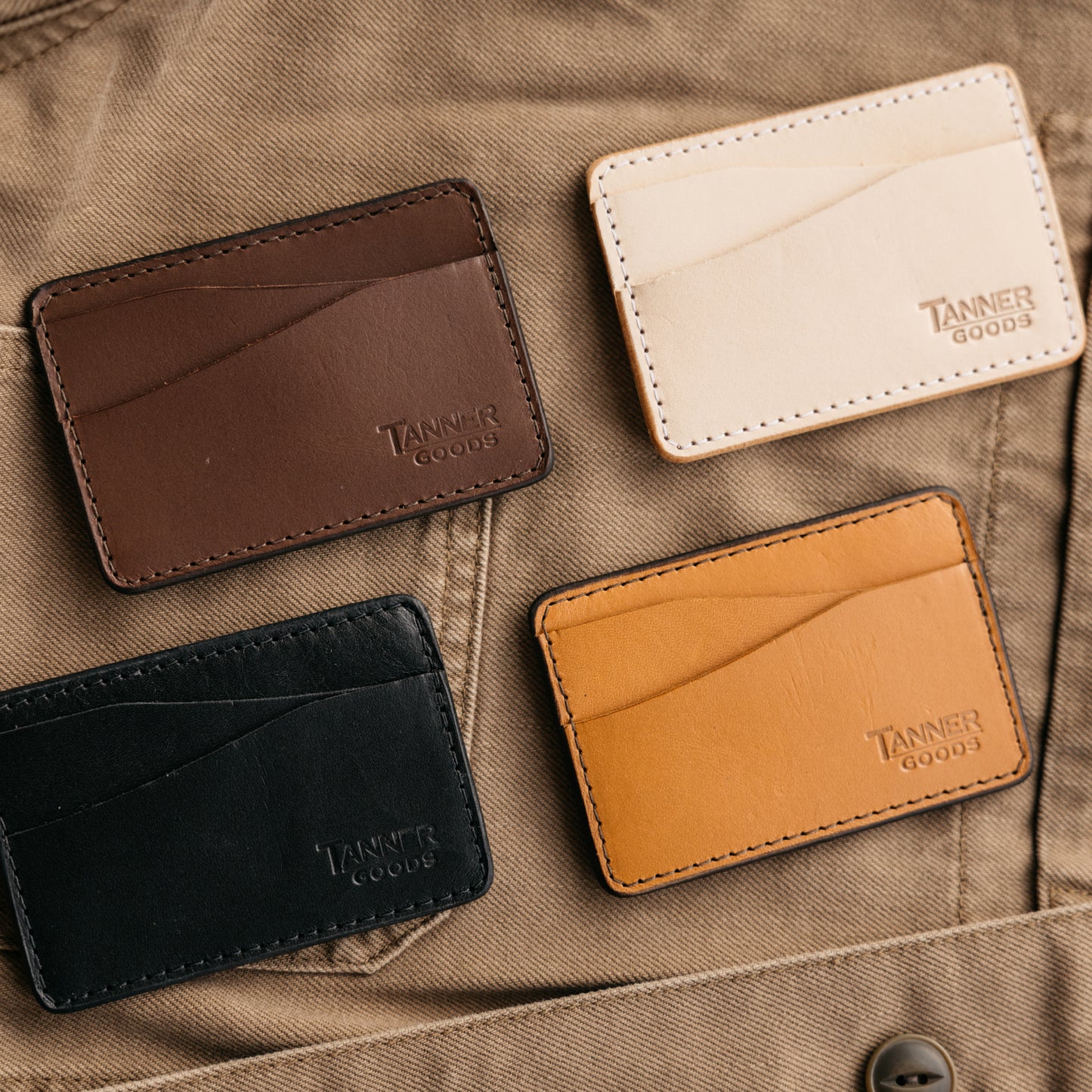 Saddle tan leather money clip wallet by Tanner Goods, displayed with three other color variations on a khaki background.