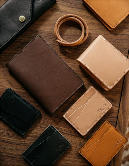 Leather wallets and cardholders in brown, black, and tan arranged on a wooden surface with a leather bracelet.