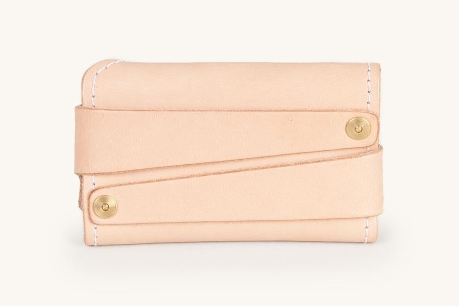 Natural leather cardholder with two diagonal straps secured by brass snaps and white contrast stitching.
