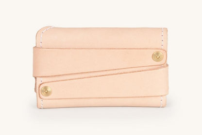 Natural leather cardholder with two diagonal straps secured by brass snaps and white contrast stitching.