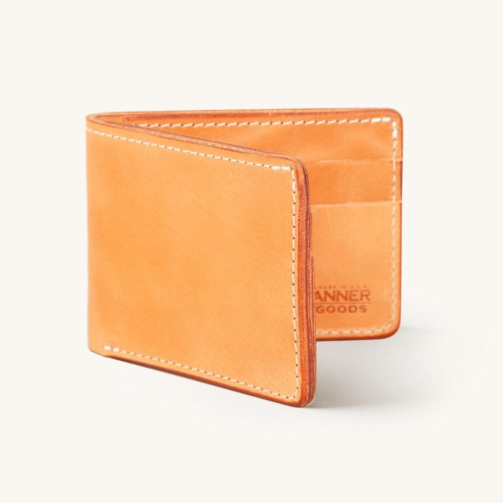 Golden leather bifold wallet standing partially open, with white stitching and a partial 'ANNER GOODS' logo inside.
