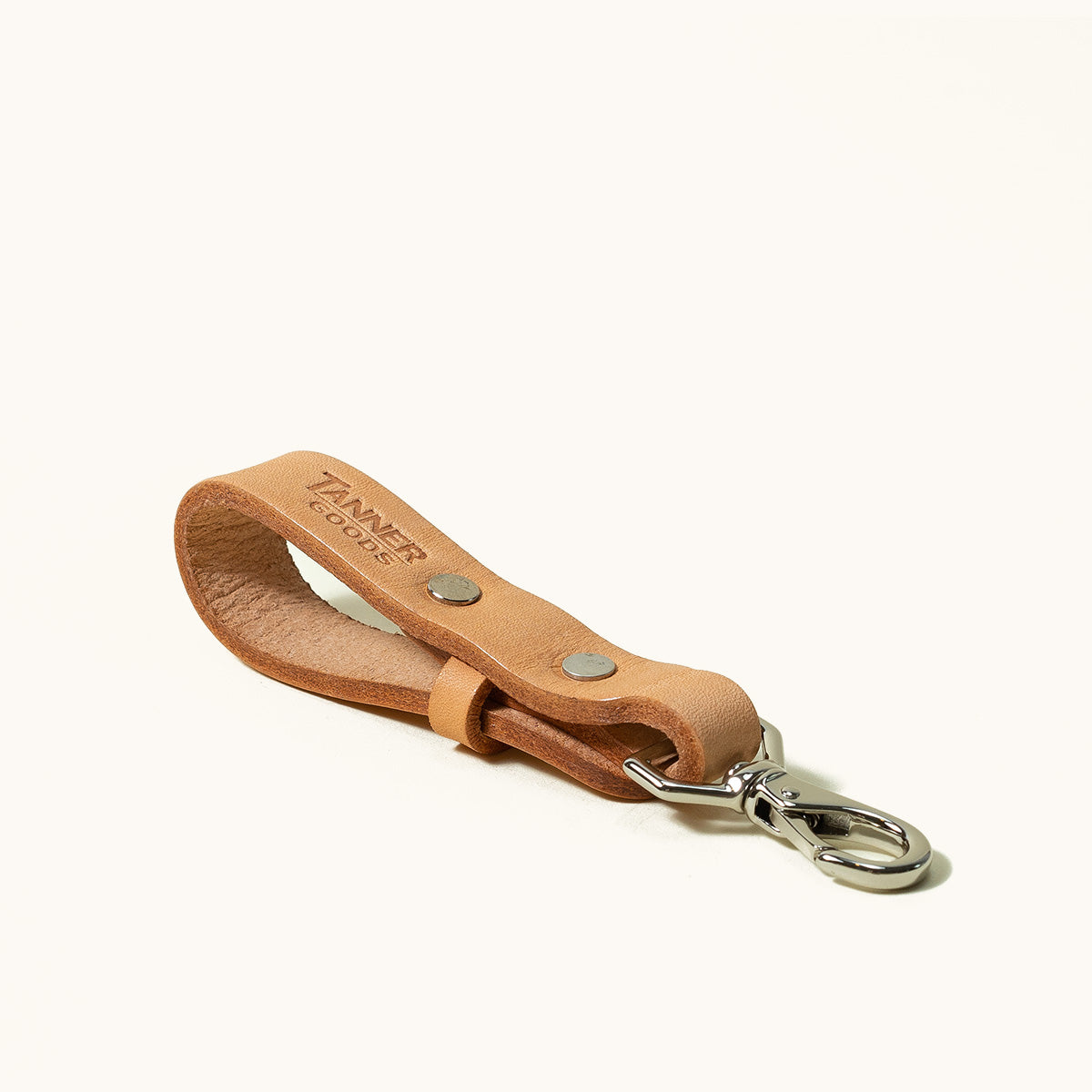 Natural leather key lanyard by Tanner Goods, with debossed logo, silver-tone carabiner, and rivets, angled on white.