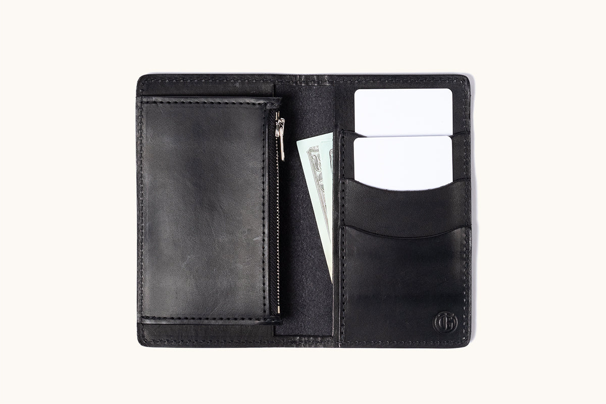 Black leather bifold wallet open to show card slots with two white cards, a zippered pocket, and a dollar bill.
