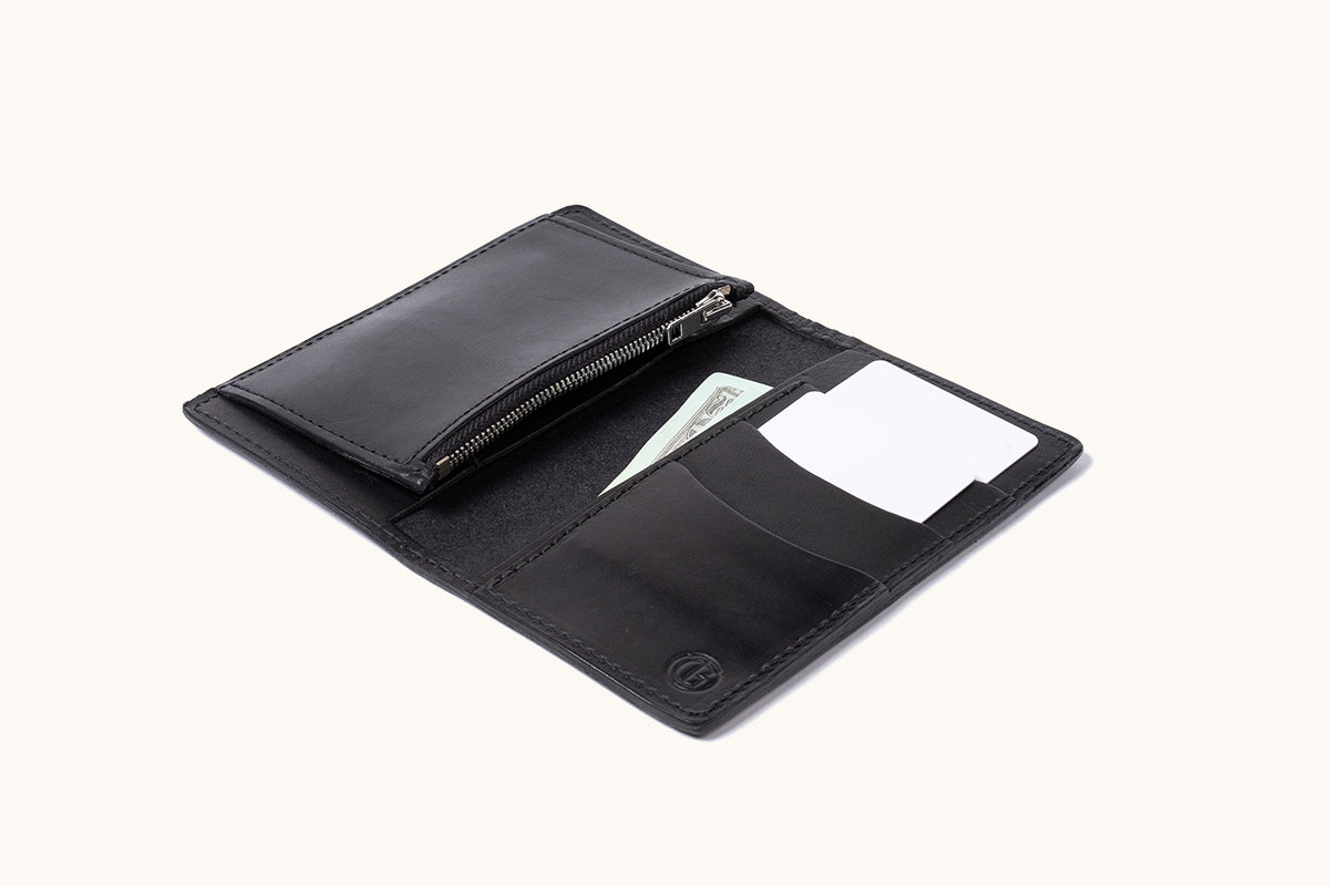Black leather bifold wallet, open to reveal a zippered pouch, card slots, a dollar bill, and two white cards.