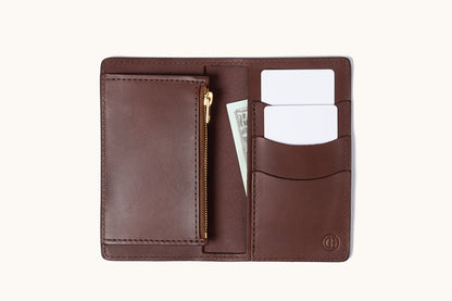 Open cognac leather bifold wallet with a gold zipper, two blank cards, and a dollar bill.