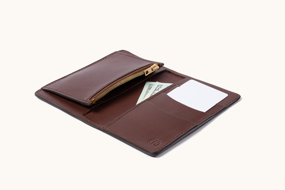 Cognac leather bifold wallet, open to reveal a zippered pocket, card slots, money, and white cards.