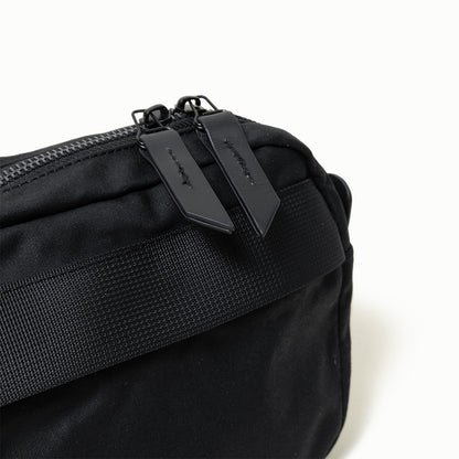 Black waxed canvas Canyon Crossbody Pack, a close-up showing two textured zipper pulls and a black webbed strap.
