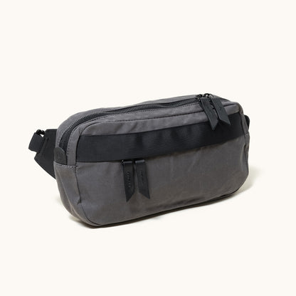 Dark grey fabric Canyon Crossbody bag with a black front strap and two zipper pulls, angled view.