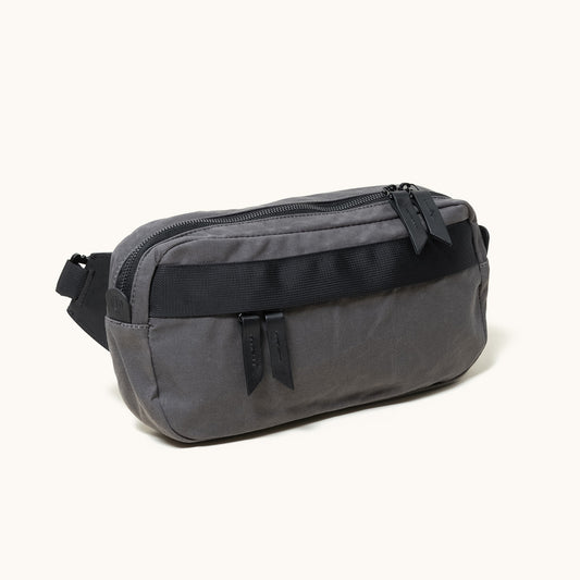 Dark grey fabric Canyon Crossbody bag with a black front strap and two zipper pulls, angled view.