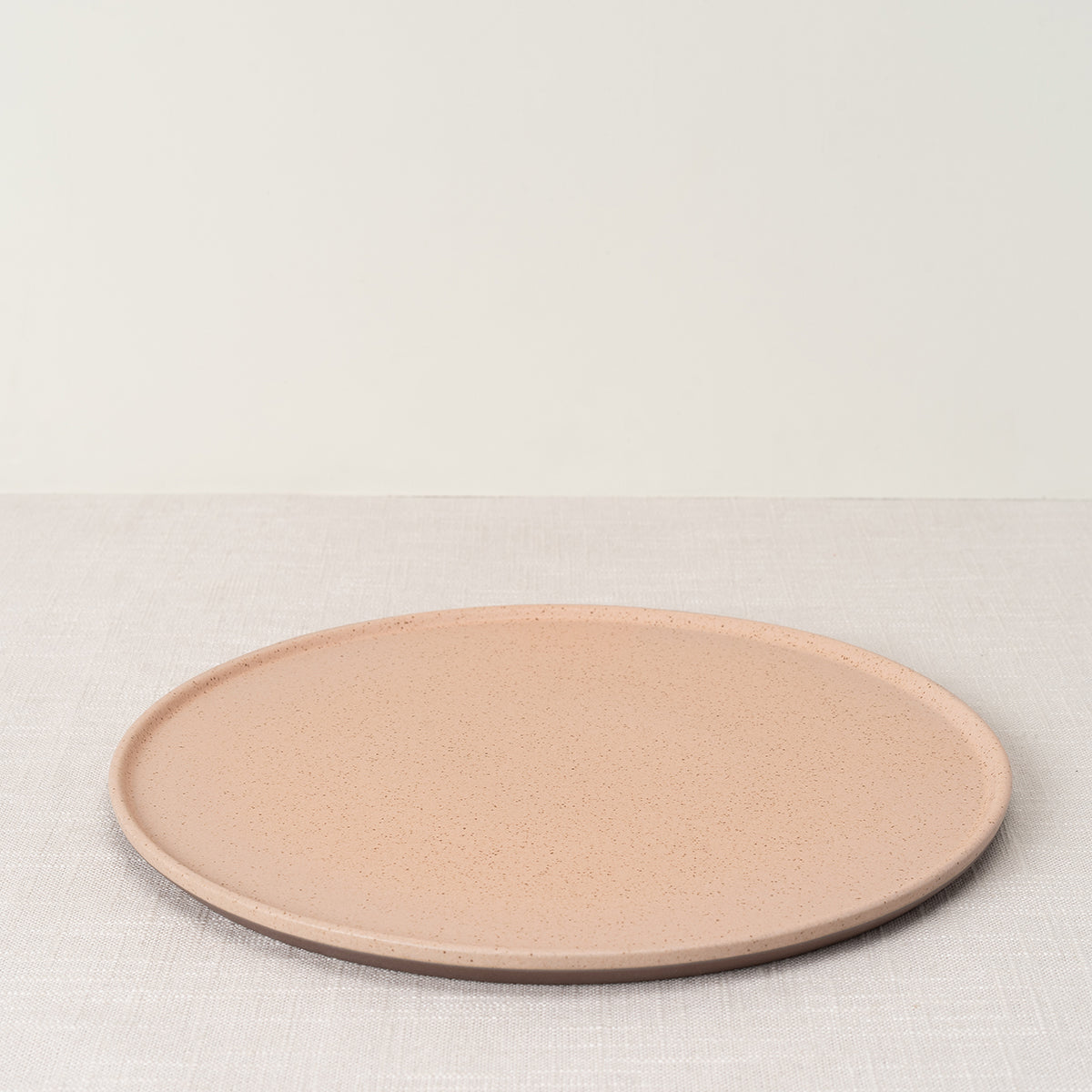 A pink speckled dinner plate resting on a light woven tablecloth.