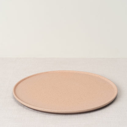 A pink speckled dinner plate resting on a light woven tablecloth.