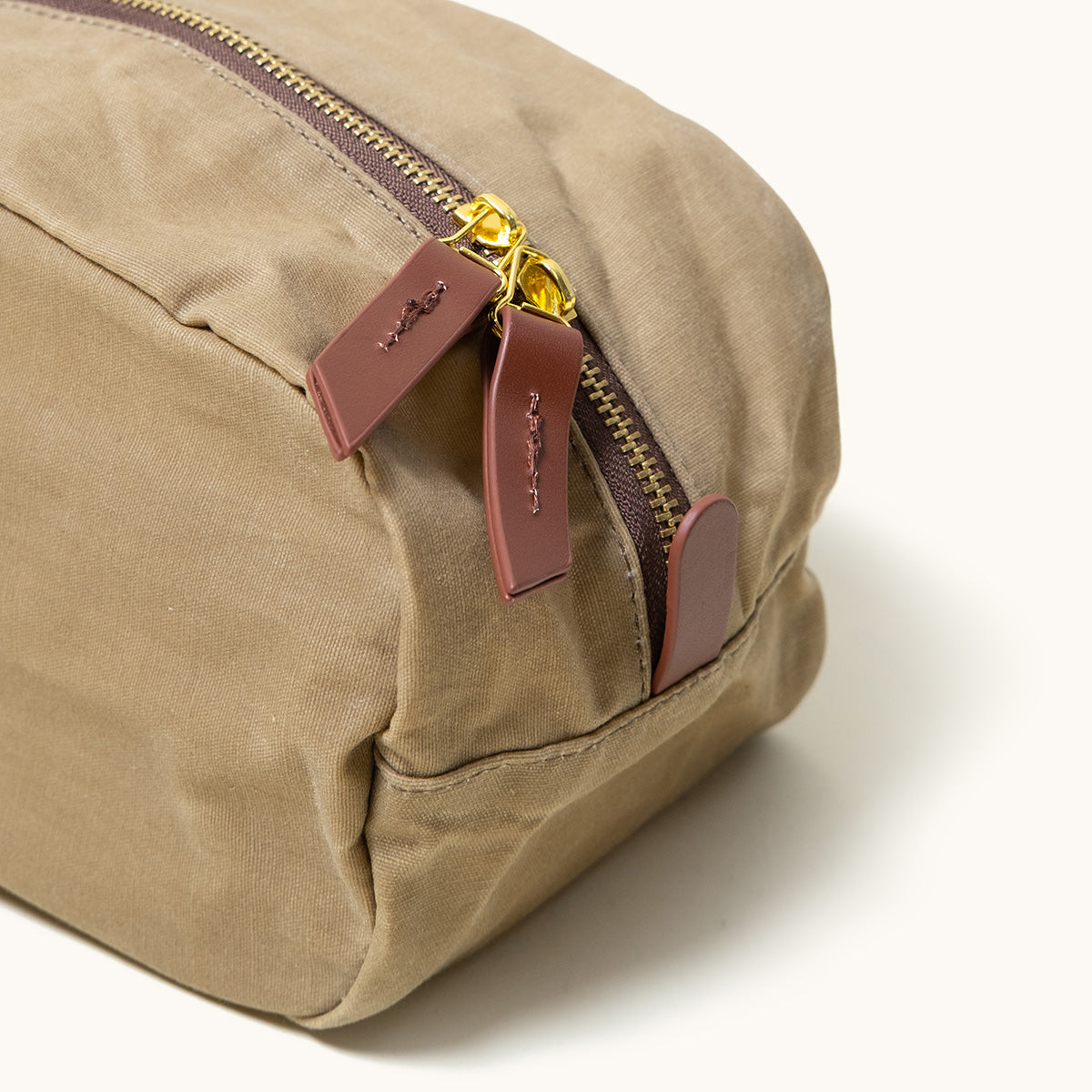 Utility tan waxed canvas Dopp Kit, cropped view, featuring a brass zipper and brown leather pull tabs with debossed detail.