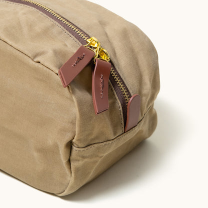 Utility tan waxed canvas Dopp Kit, cropped view, featuring a brass zipper and brown leather pull tabs with debossed detail.