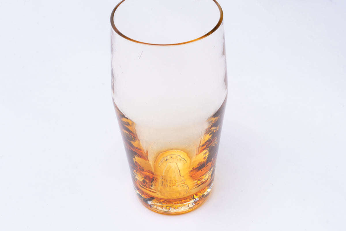 Amber-tinted glass pint with a detailed bottom embossment and a clear upper section, angled view.