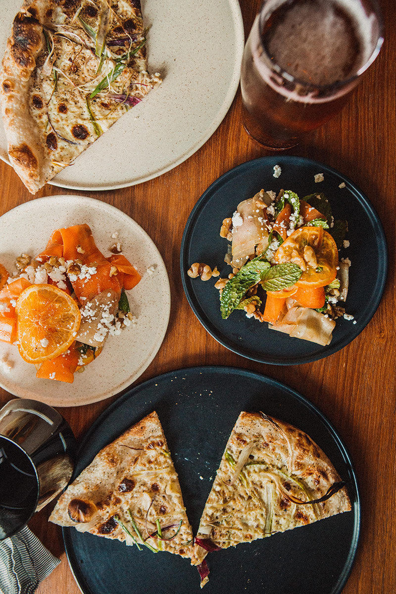 Rosado ceramic side plates with a speckled texture, round and styled with food on a wooden table.