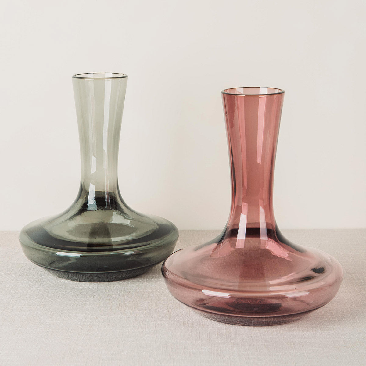 Two glass decanters, one grey and one plum, with wide bases and tall, narrow necks.