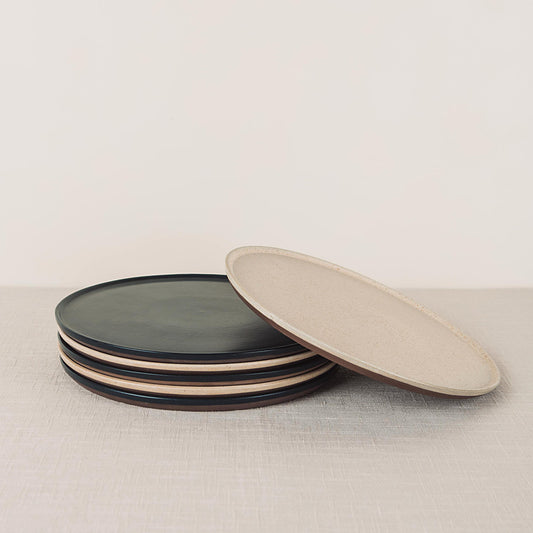 Stacked dark gray round dinner plates and an oval beige speckled plate with brown rims.
