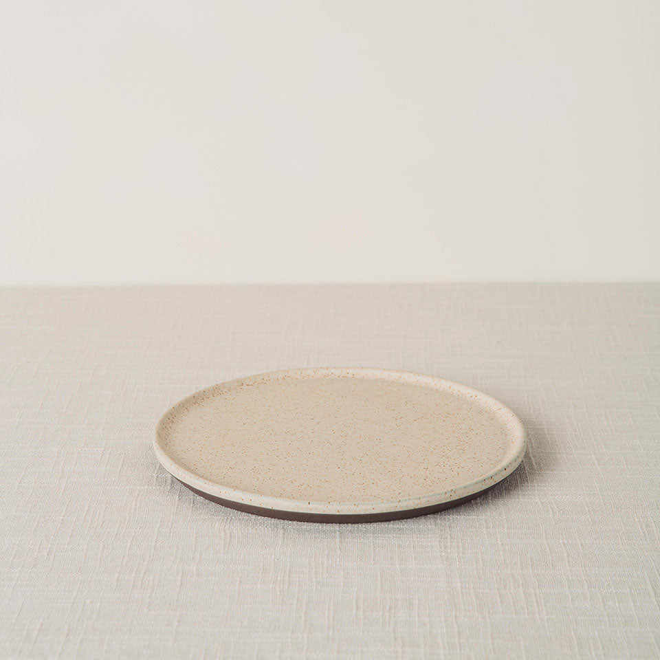 Sandstone side plate with a speckled cream surface and dark brown base, angled on a light linen tablecloth.