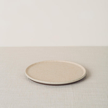 Sandstone side plate with a speckled cream surface and dark brown base, angled on a light linen tablecloth.