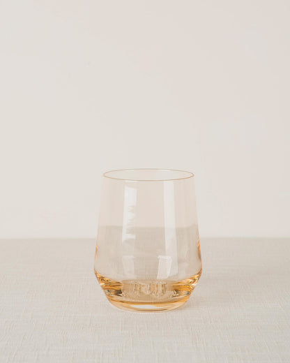 Pale amber stemless wine glass with a thick patterned base, resting on a light linen surface.