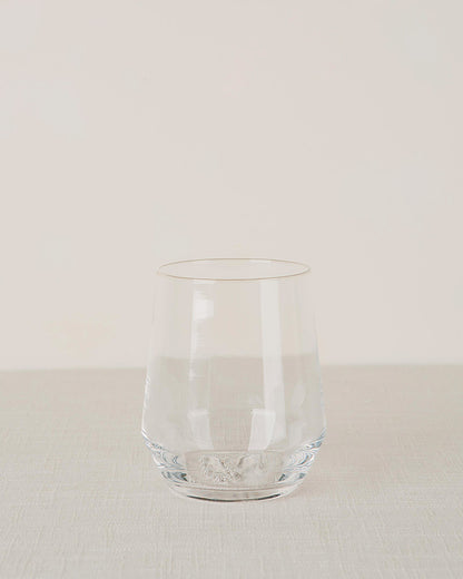 Clear stemless wine glass on a light textured surface with a plain background.