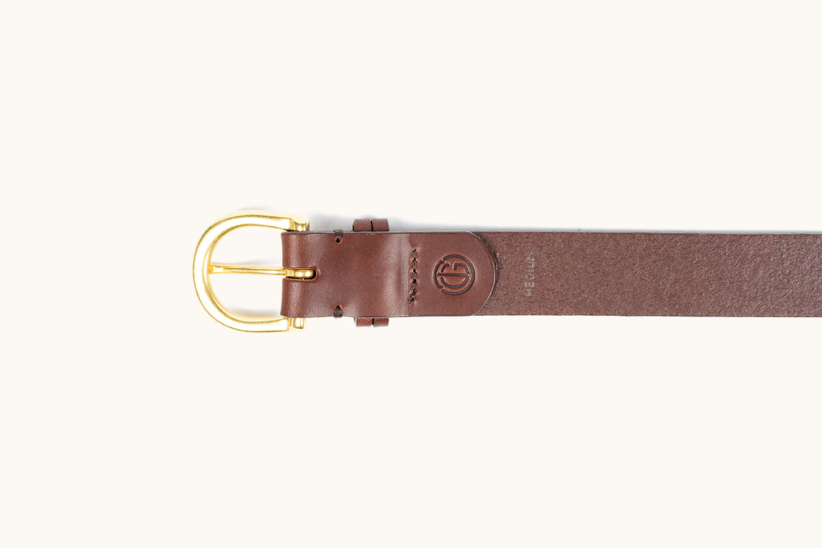 Cognac leather belt with a gold-toned buckle, embossed logo, and "MEDIUM" text, laid flat.