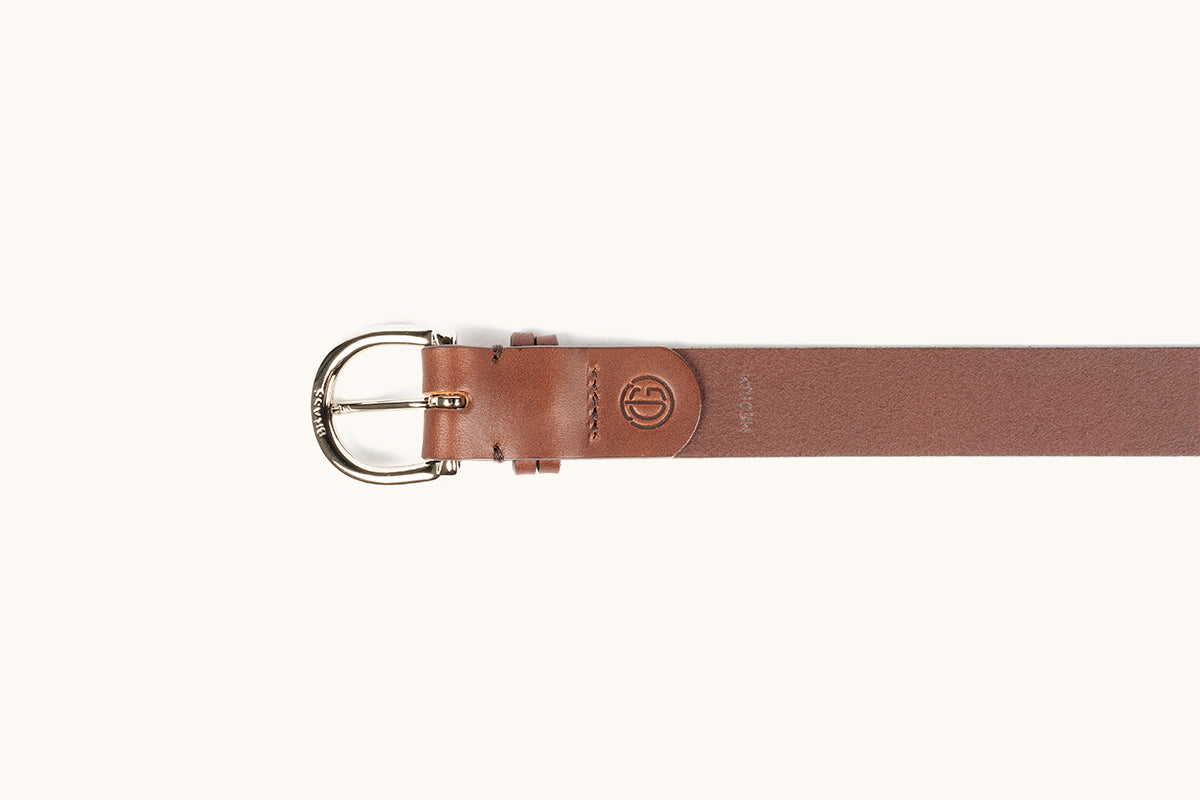 A cognac brown leather belt with a polished silver-toned buckle engraved "BRASS" and an embossed circular logo.