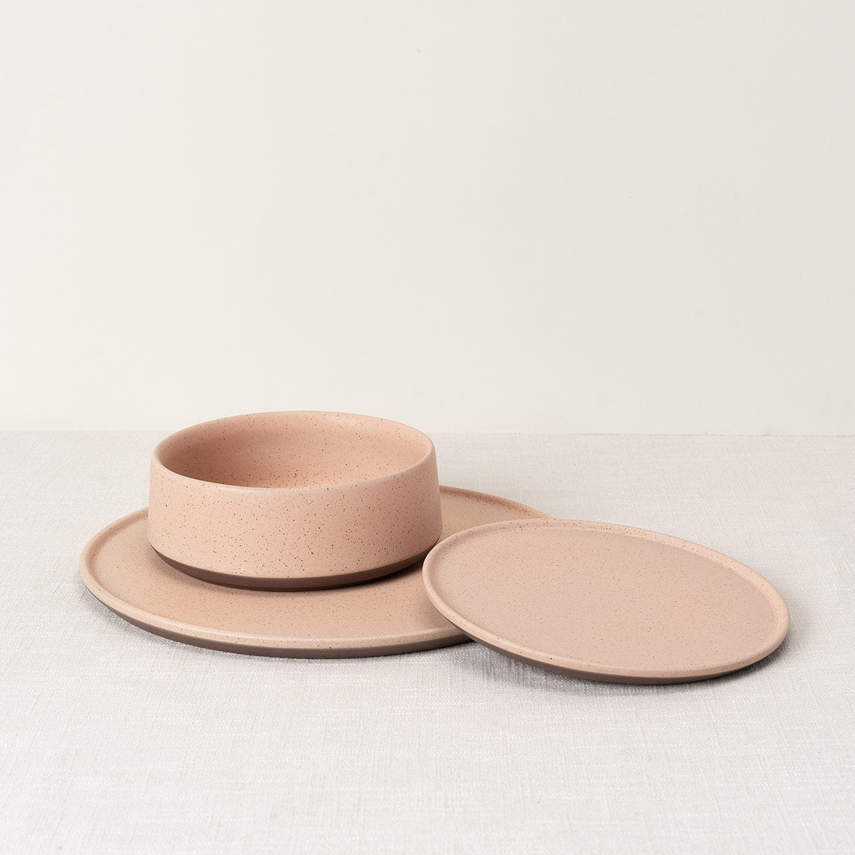 Speckled light pink oval side plate, part of a ceramic set with a bowl and round plate.