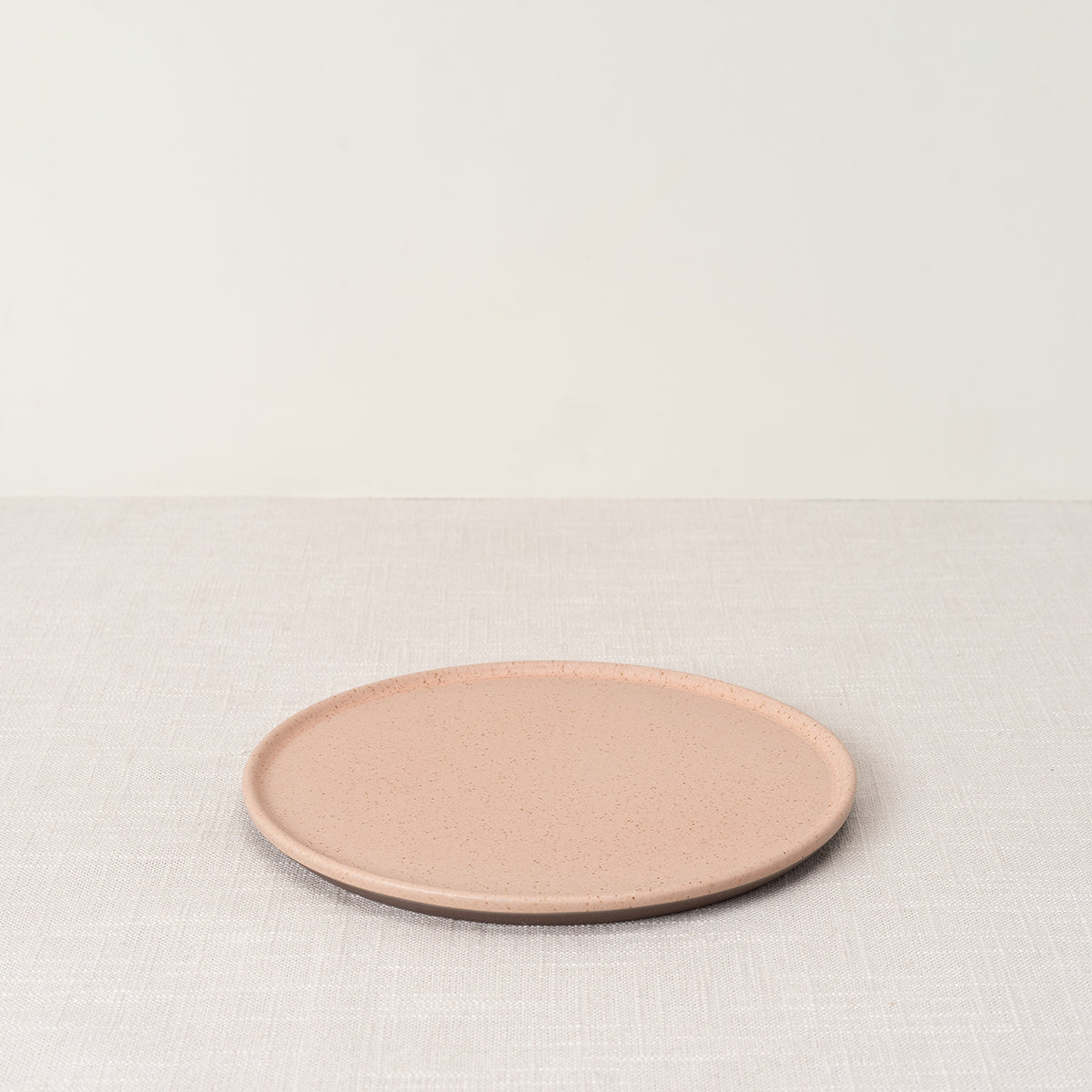 Rosado side plate with speckled pink surface and dark brown rim, on a light textured tablecloth.