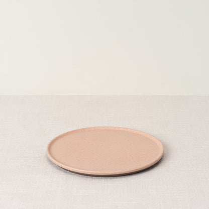 Rosado side plate with speckled pink surface and dark brown rim, on a light textured tablecloth.