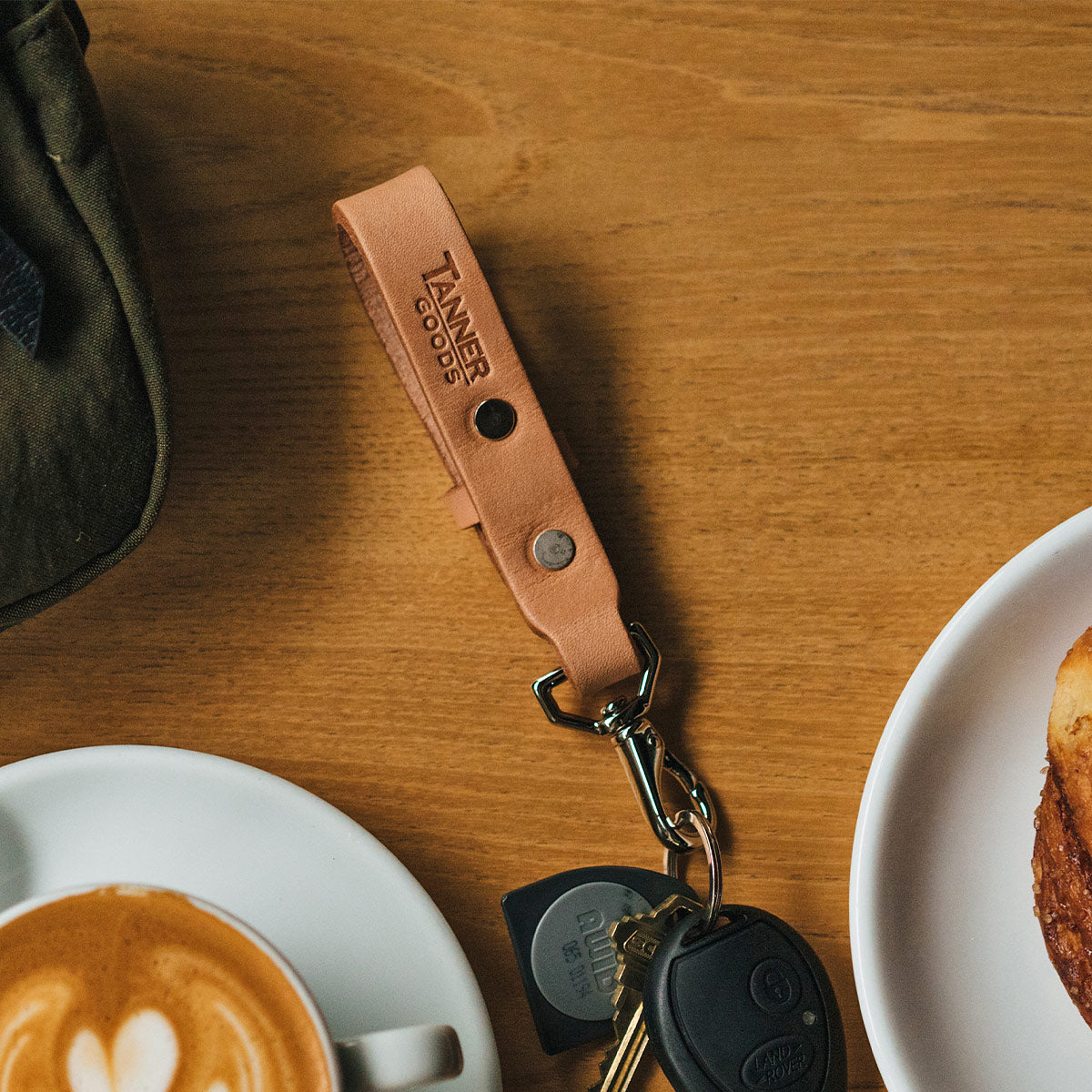 Natural leather key lanyard by Tanner Goods, with a metal clasp and car keys on a wooden table.