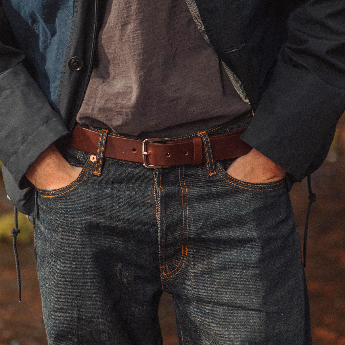 Cognac leather belt with a silver-toned buckle, styled with dark blue jeans and a grey t-shirt on a person.