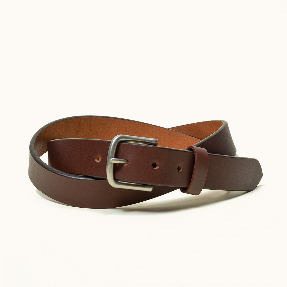 Classic cognac leather belt with a silver-toned buckle, coiled on a light background.