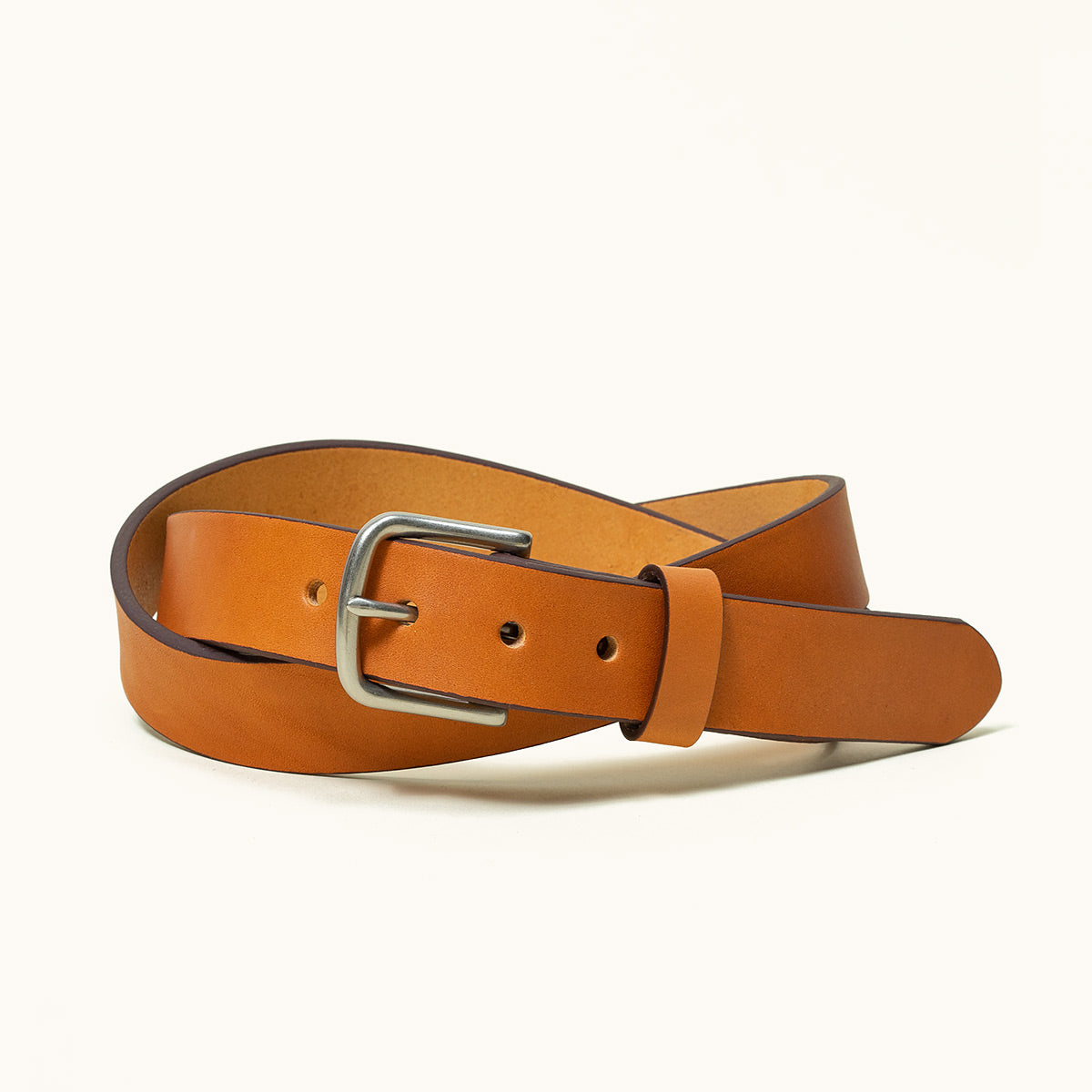 Saddle tan leather classic belt with a silver-tone buckle, coiled.