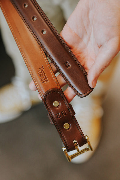 Cognac leather dress belt and a dark brown belt with brass buckles, stamped with 'TANNER GOODS', 'DAD', and '32'.