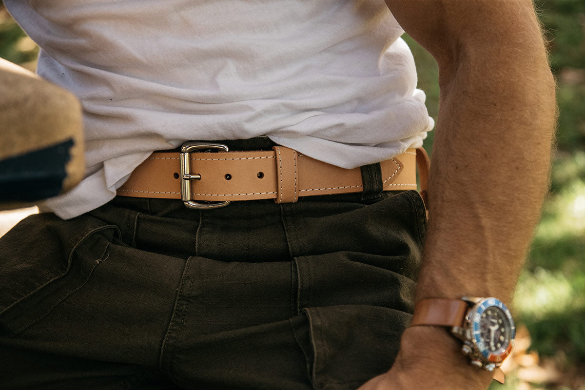 Natural leather Heritage belt with a silver-tone buckle, white stitching, worn with dark green pants and a watch.
